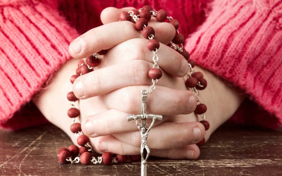 child holding rosary beads with hands crossed