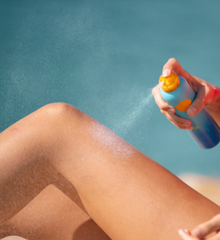 Person spraying sunscreen on their leg