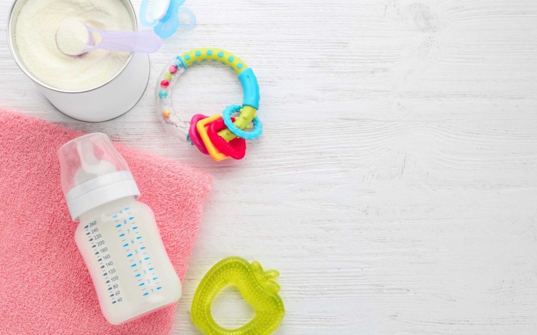 baby formula in a bottle with a pink towel and baby toys next to a can of infant formula mix